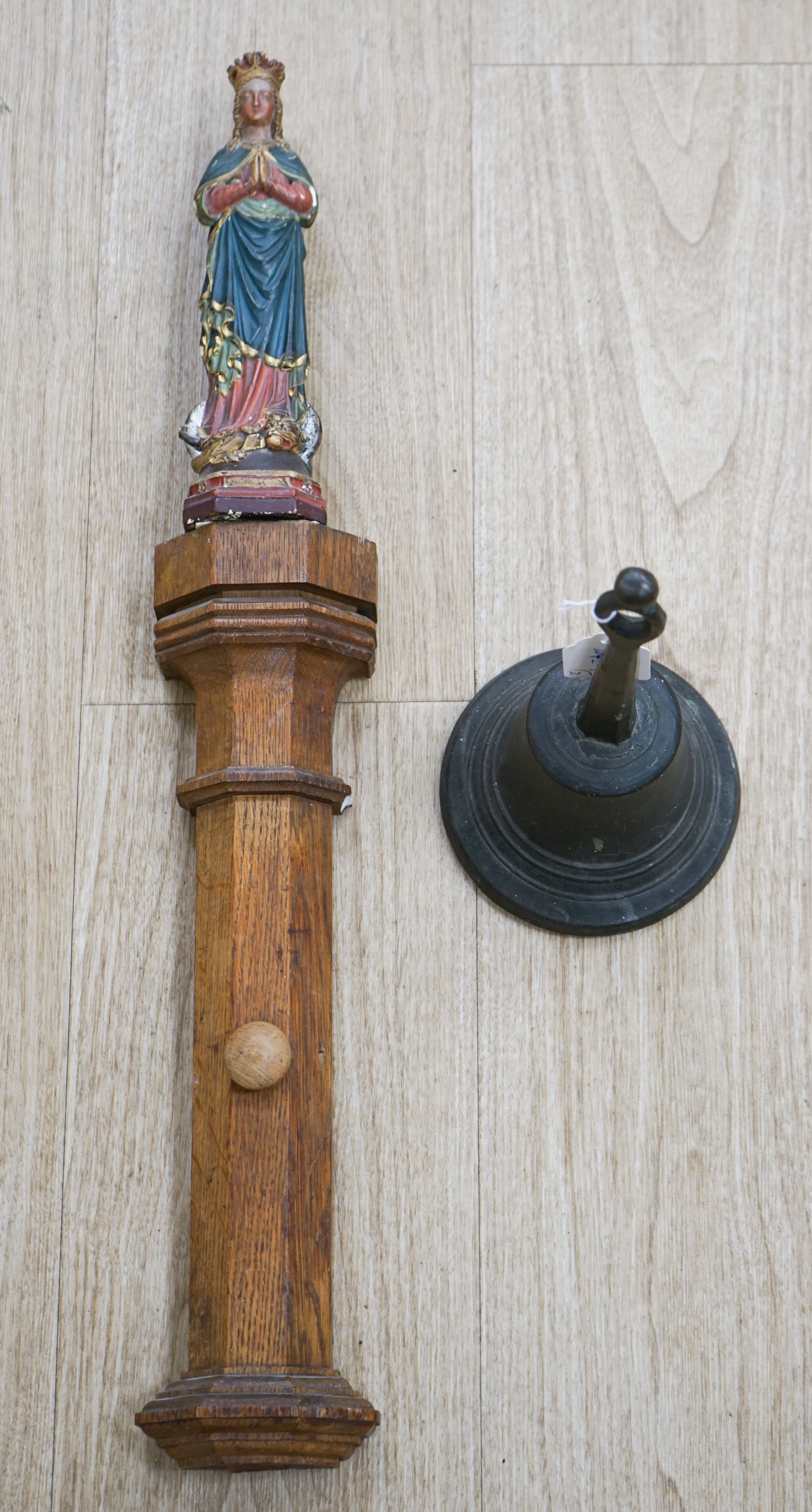 An early hand bell and a religious figure on an oak pilaster 65cm